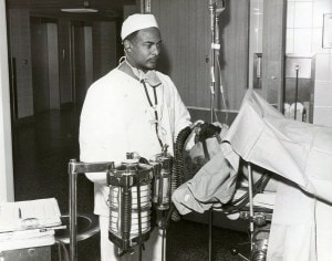 African American doctor in vintage photo, wearing whites with stethoscope around his neck studying medical equipment
