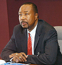African American man in business suit and tie, sitting at a desk with hands resting on the desk clasped in front of him